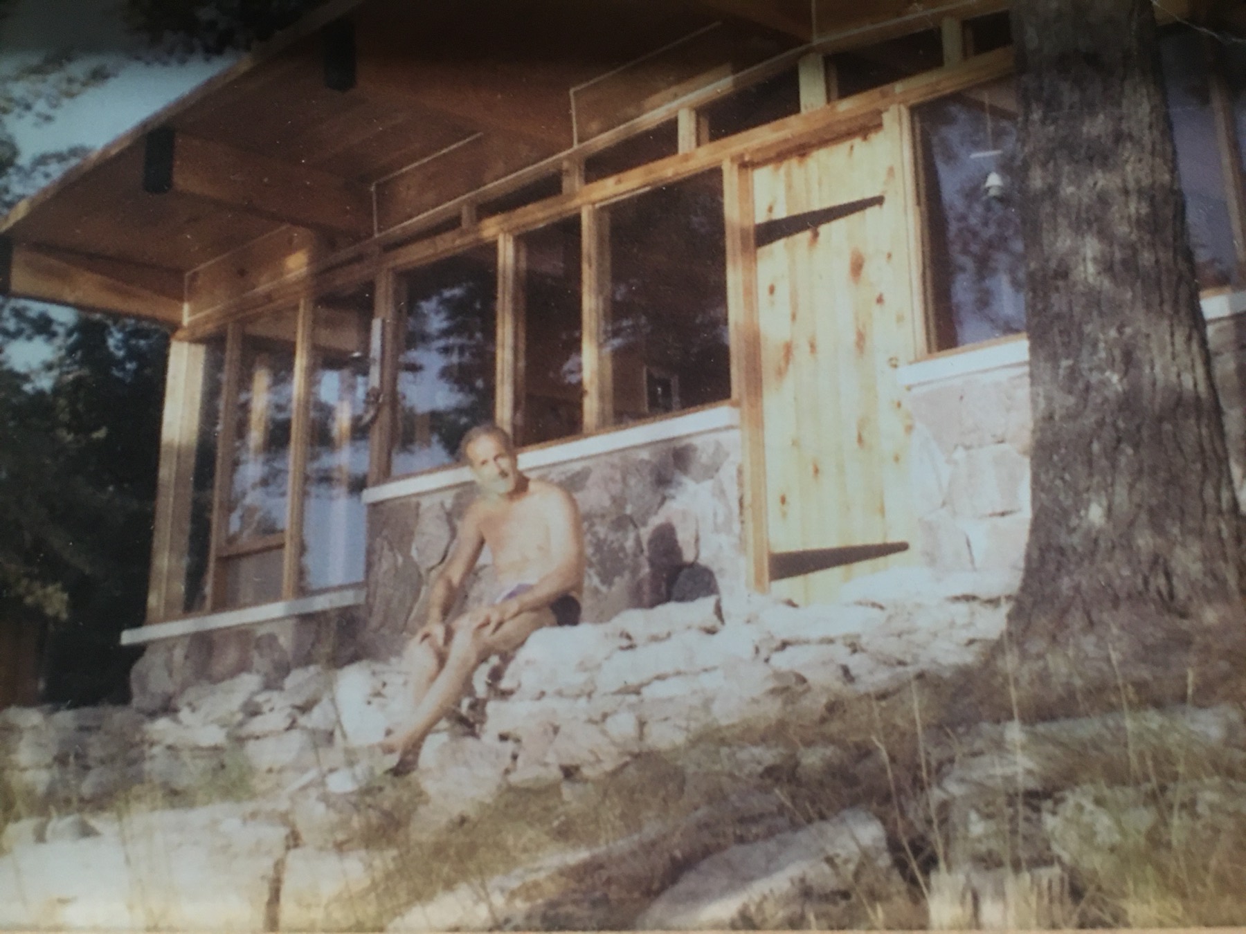 Reg Wheeler seated on the stone foundation of the cottage he built, Kawartha Lakes, 1961.
